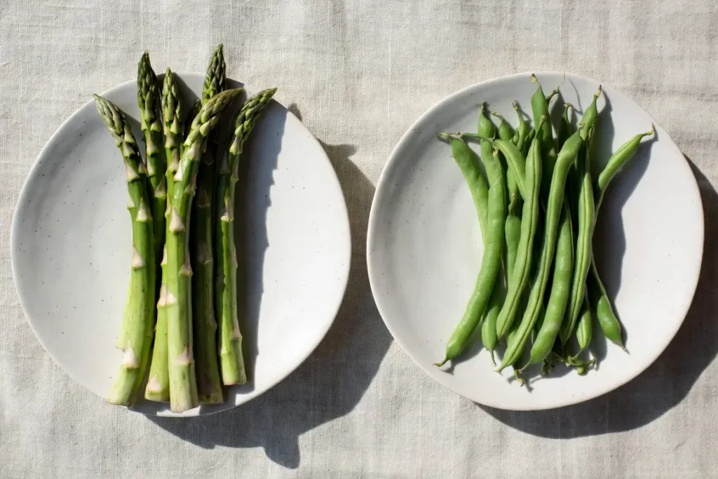 Asparagus and green beans side by side, photographed for nutritional comparison