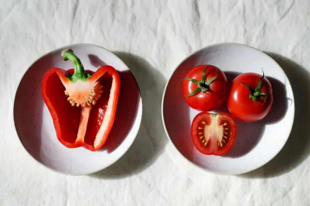 Red bell pepper and tomato side by side, photographed for nutritional comparison